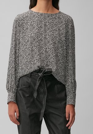 Top a fiori in bianco e nero con maniche lunghe e scollatura rotonda, abbinato a pantaloni in pelle nera a vita alta con cintura annodata.