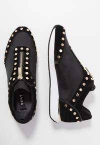 Svarta sneakers med en kombination av slät tyg och mocka. Har guldnitar, en dragkedja i mitten och en vit sula. Strukturerad design över hela ytan.