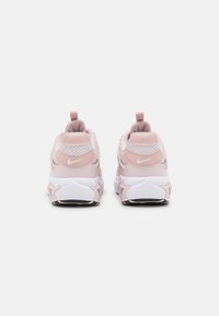 Nike sneakers in light pink with mesh and synthetic upper, white midsole, and textured rubber outsole. Heel pull tab for easy wearing.