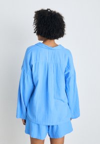 Cămașă din bumbac de culoare albastru deschis, cu o croială lejeră, mâneci lungi și guler pliat. Spatele are un pli delicat pentru un plus de textură.