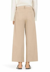 Beige wide-leg trousers with a high waist, back pockets, and a smooth texture, paired with simple sandals.