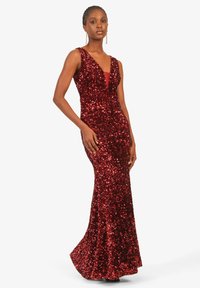 Rote Pailletten-Abendkleid mit tiefem V-Ausschnitt, tailliertem Oberteil, ausgestelltem Saum und einer transparenten inneren Schicht. Glänzende, strukturierte Oberfläche und ärmelloses Design.