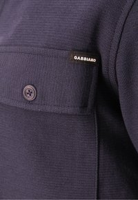 Donkerblauwe gebreide stof met een borstzak met knopen, voorzien van een zwart label met de tekst "GABBIANO".
