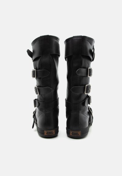 Ζευγάρι ψηλές μαύρες δερμάτινες μπότες με τρεις λουράκια με αγκράφες στην πίσω πλευρά και μια μικρή καφέ ετικέτα κοντά στη σόλα.