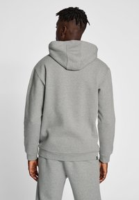 Grå hoodie i mjukt material, med en stor huva, ribbade ärmslut och midja. Enkel, neutral design utan mönster eller detaljer.