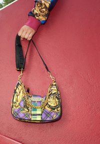 Borsa in stile hobo con dettagli in catena dorata, motivi scozzesi viola e verde, e decorazioni floreali; dotata di una tracolla nera regolabile.