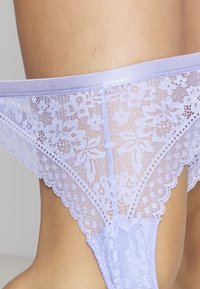 Spetstrosa i ljus lavendel med blomstertryck, scallopade kanter och midjeband i satin. Har genomskinliga detaljer och en figurnära passform.