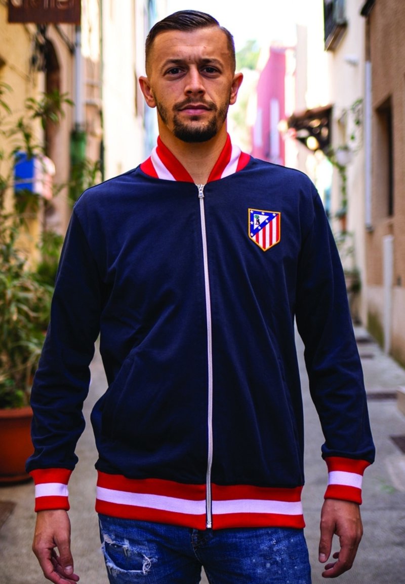 Marine blauwe zip-up jas met rode en witte gestreepte accenten. Bevat een clublogo op de linkerborst en heeft een zachte textuur.