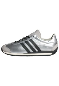 Silver athletic shoe with a smooth leather upper, black three-stripe design, black laces, and a white sole; rounded toe and padded collar.