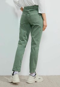 Pantalones tapered de color verde claro con una cinturilla elástica y bolsillos en la parte posterior, combinados con zapatillas blancas y negras. La textura parece suave.