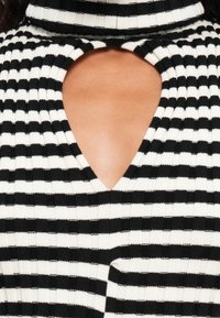 Pletena majica s crno-bijelim prugama s visokim ovratnikom i izrezom u obliku ključa na izrezu, koja ističe rebrastu teksturu.