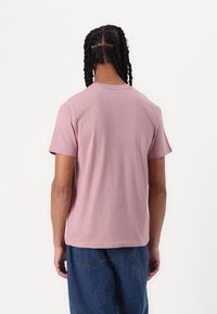 T-shirt de manga curta, rosa claro, com colarinho redondo. Tecido de algodão suave, corte casual, com costuras visíveis e uma bainha reta.