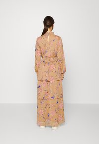 Vestido maxi com padrões florais em bege, apresentando mangas longas, cintura ajustada e uma abertura em forma de olho-chave nas costas. Design em camadas subtil.