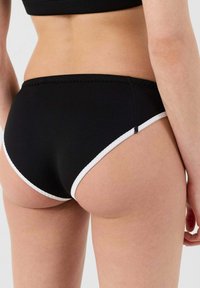 Costumi da bagno neri con bordi bianchi, caratterizzati da una texture liscia, design a vita bassa e dettagli di cucitura. Adatti per nuotare o per la spiaggia.