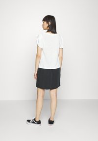 Top branco de manga curta com um corte solto, combinado com uma saia preta até ao joelho. O modelo usa ténis pretos com solas brancas.