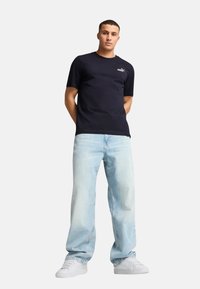 Marineblauwe katoenen T-shirt met korte mouwen en een subtiel logo op de borst, gecombineerd met lichtblauwe baggy jeans en witte sneakers.