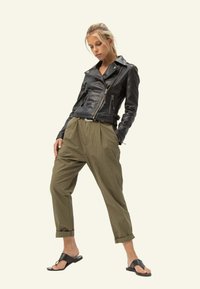 Czarna skórzana kurtka motocyklowa z zamkami, luźne oliwkowe spodnie i czarne klapki, na neutralnym tle.