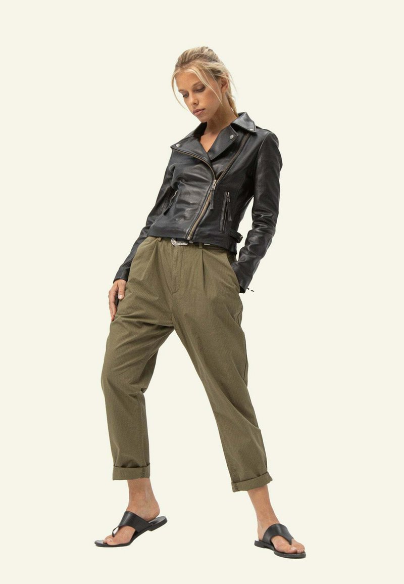 Czarna skórzana kurtka motocyklowa z zamkami, luźne oliwkowe spodnie i czarne klapki, na neutralnym tle.