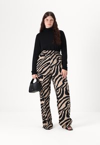 Svart langermet topp med høy hals, kombinert med beige bukser med svarte zebra-striper. Modellen holder en svart håndveske.