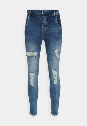 Blå skinny jeans med slidte huller foran på lårene og knæene, forlommer og knaplukning i taljebåndet.