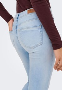 Ανοιχτό μπλε τζιν παντελόνι με στενή γραμμή, με πίσω τσέπες, ταμπέλα σε ταμπά χρώμα στη μέση και διακριτική φθορά λεπτομερείες.