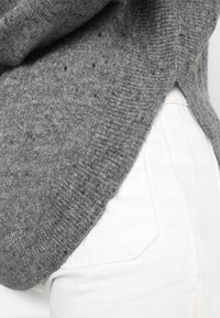 Maglione grigio lavorato a maglia con un design morbido, caratterizzato da un orlo a coste e un tessuto testurizzato, abbinato a pantaloni in denim bianchi.