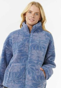 Veste en polaire bleue avec fermeture éclair à l'avant, col haut, et deux poches avant ; présente un motif texturé et un tissu doux et duveteux.