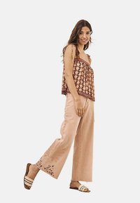 Top fluido con estampado y tirantes finos, combinado con pantalones de pierna ancha en rosa pálido que presentan bordados florales, y sandalias planas con tres tiras.
