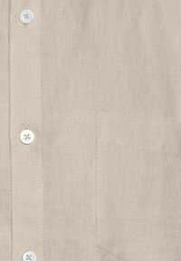 Beige linned skjorte med knaplukning foran, en lappelomme på brystet og hvide knapper. Stoffet har en tekstureret overflade.