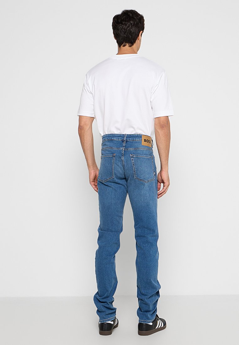 Niebieskie dżinsy z prostym krojem nogawki, z brązową skórzaną naszywką na tylnej części pasa i dwiema tylnymi kieszeniami. Styl casual.