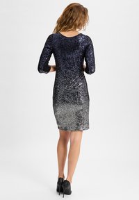 Knee-langes Kleid mit einem Paillettendesign, das einen Farbverlauf von dunkelblau zu silber aufweist. Lange Ärmel und eine taillierte Silhouette. Schwarze Absätze.