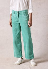 Groene corduroy wijde broek met een geweven afwerking, voorzien van een knoopsluiting en zijzakken. Gecombineerd met witte sneakers.