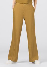 Gula vida byxor i lättviktig tyg, med fickor, hög midja och slät yta. Matchas med vita sneakers.