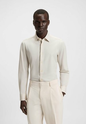 Ljus beige l�ångärmad skjorta med mjuk textur, knäppt fram och spetsig krage, i kombination med matchande byxor.
