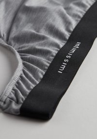 Grå elastisk stofundertøj med en glat overflade, med en sort elastik med hvid broderet tekst.