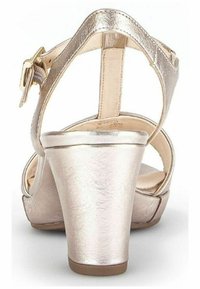 Sandales à talons en rose gold avec une finition métallique brillante, dos ouvert, bride de cheville et semelle plateforme. Le talon est épais et texturé.