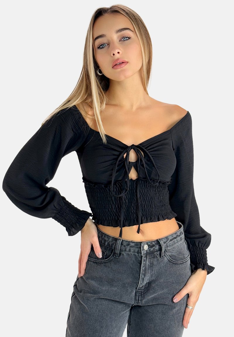 Top corto nero con scollatura a spalle scoperte, texture smock e dettaglio di nodo frontale. Maniche lunghe e arricciate completano il design.