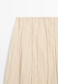 Beige, let plisseret nederdel med rynket taljebånd vist på en flad, hvid baggrund.