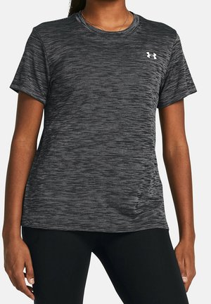 Kobieta nosząca sportową, krótką koszulkę w ciemnoszare paski z małym białym logo Under Armour na piersi.