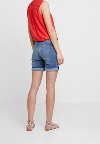 Denim shorts with rolled hems, high waist, and back pockets, paired with a red sleeveless top and silver strappy sandals.