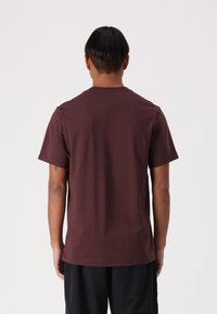 T-shirt en coton bordeaux avec un col rond, des manches courtes et une coupe décontractée. Texture lisse, sans motifs ni accents visibles.