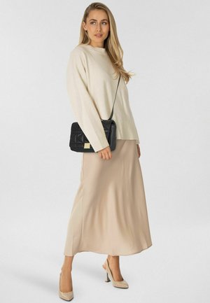 Crèmekleurige gebreide trui met geribbelde manchetten, beige satijnen maxirok, zwarte gestikte crossbodytas met gouden accenten en naaldhakken in nude kleur.
