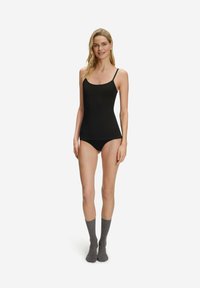 Top nero senza maniche con spalline sottili, abbinato a biancheria intima nera e calzini grigi, caratterizzato da un design aderente e una texture liscia.