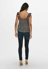 Top floreale con spalline arricciate, sfondo nero, tessuto leggero, vestibilità ampia, abbinato a jeans skinny scuri e tacchi beige.