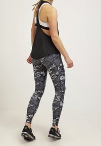 Černá top bez rukávů s designem racerback a šedé legíny s maskáčovým vzorem. Černé sportovní boty dokončují celý outfit.