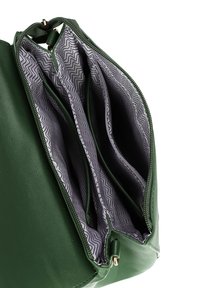 Zelená kožená kabelka se zipovým otvorem, obsahující více přihrádek podložených šedou látkou se zigzagovým vzorem.