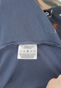Blue cotton fabric with care label. The label shows washing instructions in multiple languages. Seam detail is visible along the edge.
