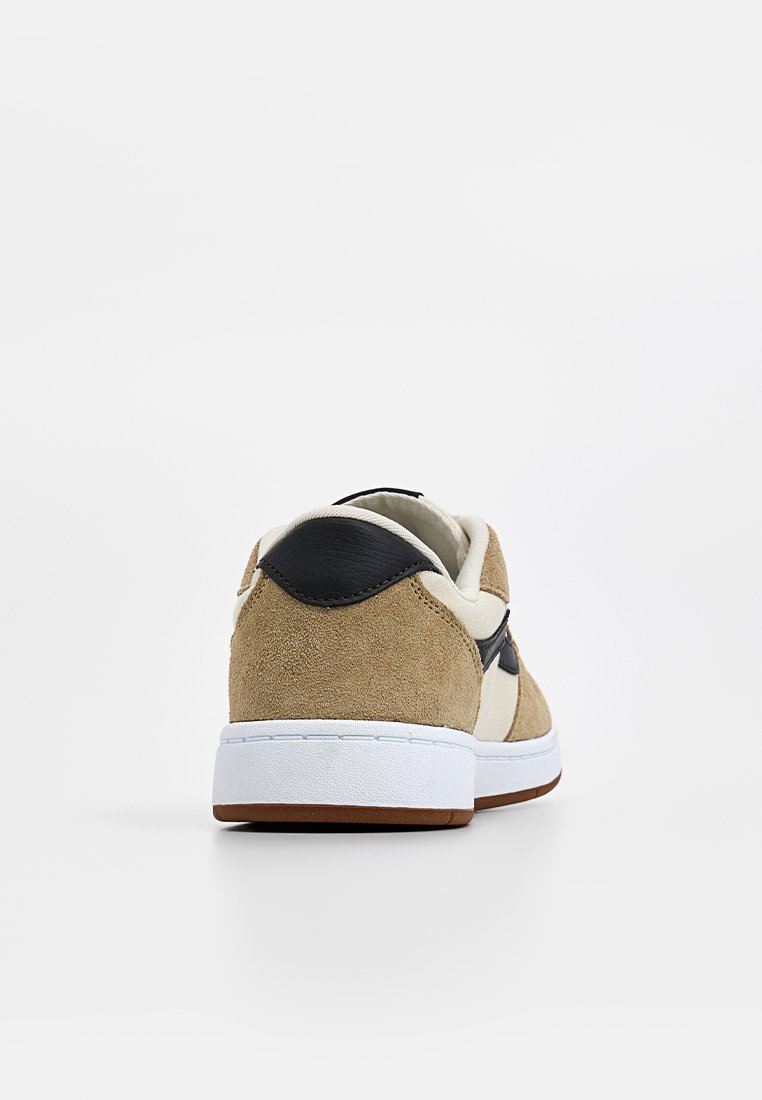 Baskets en suède beige avec des accents noirs et une semelle blanche ; présentent une forme arrondie et un design minimaliste, mettant en valeur des détails cousus.