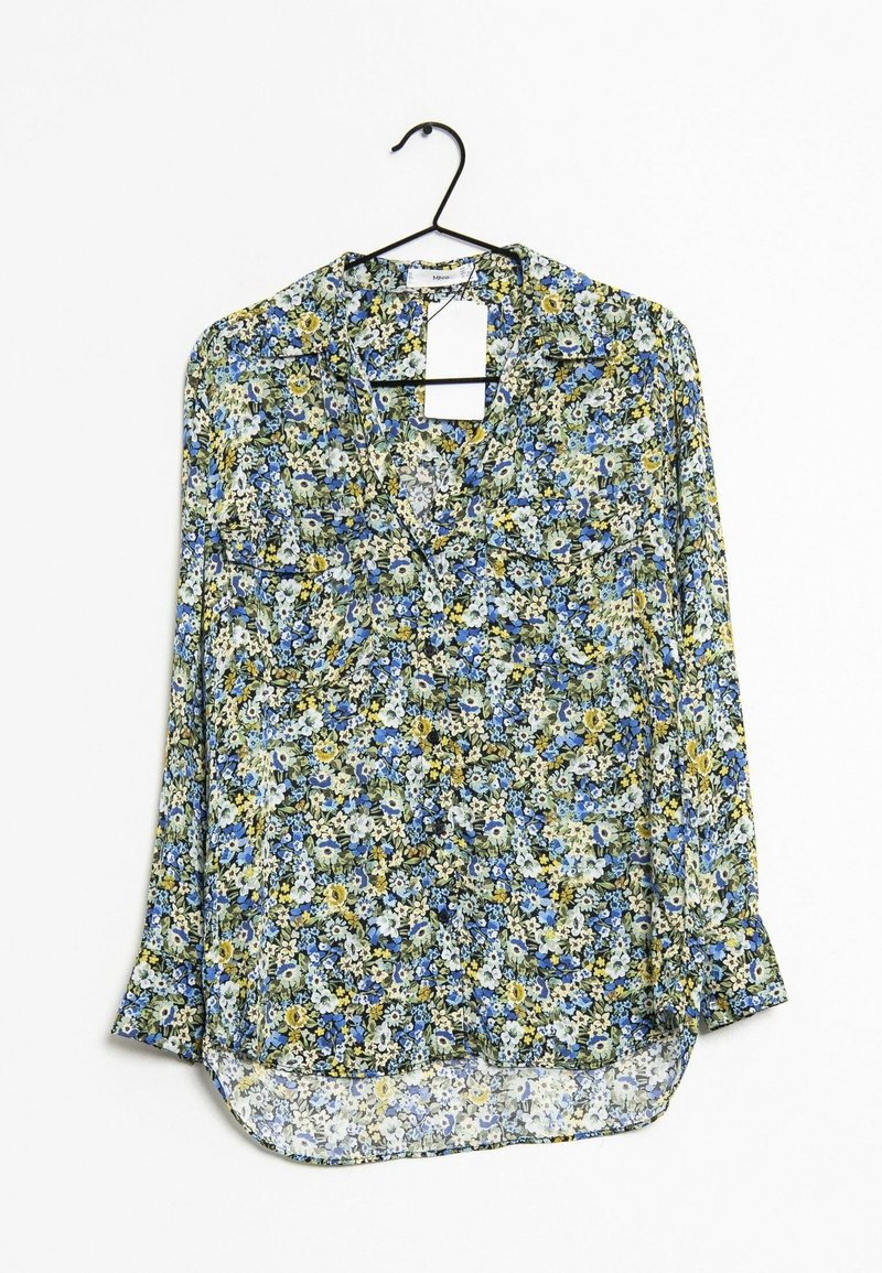 Blouse à manches longues fleurie avec des fleurs bleues, jaunes et blanches suspendue sur un cintre noir sur fond blanc.