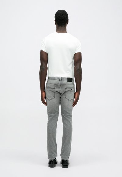 Γκρι τζιν παντελόνι με σχέδιο ευθείας γραμμής, δύο πίσω τσέπες με κεκλιμένα καπάκια και μια μαύρη δερμάτινη επένδυση στη μέση. Φορεμένο με ένα λευκό T-shirt.